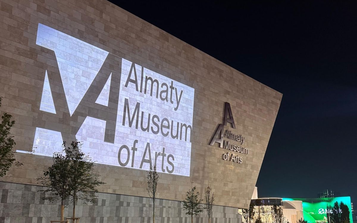 Логотип Almaty Museum of Arts, спроецированный на известняковый фасад музея вечером
