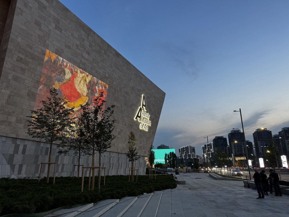 Репродукция картины и логотип Almaty Museum of Arts, спроецированные на каменный фасад музея в сумерках
