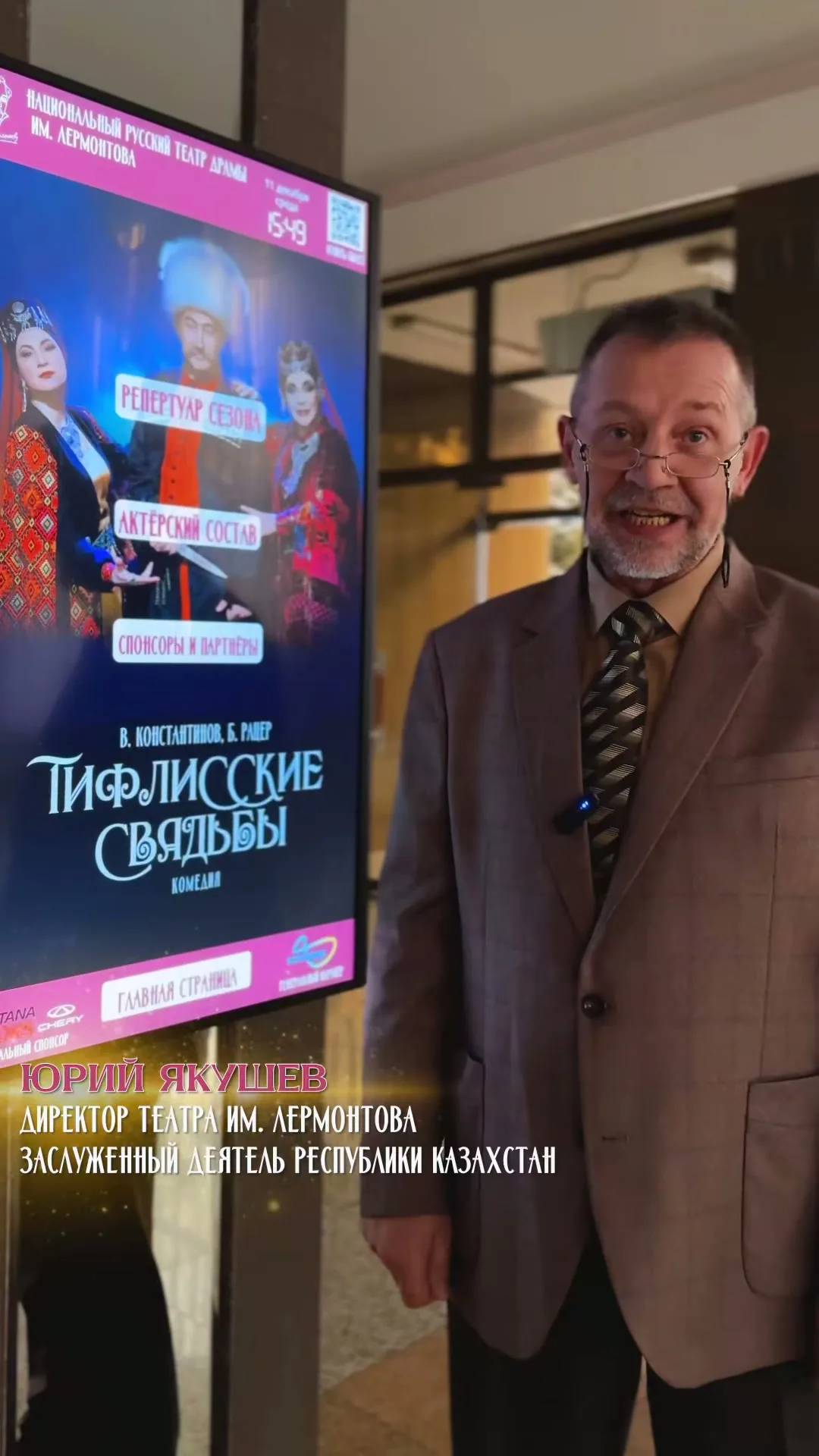 Юрий Якушев, директор театра имени Лермонтова, рядом с сенсорной панелью в фойе: на экране афиша спектакля «Тифлисские свадьбы» и три кнопки главного экрана